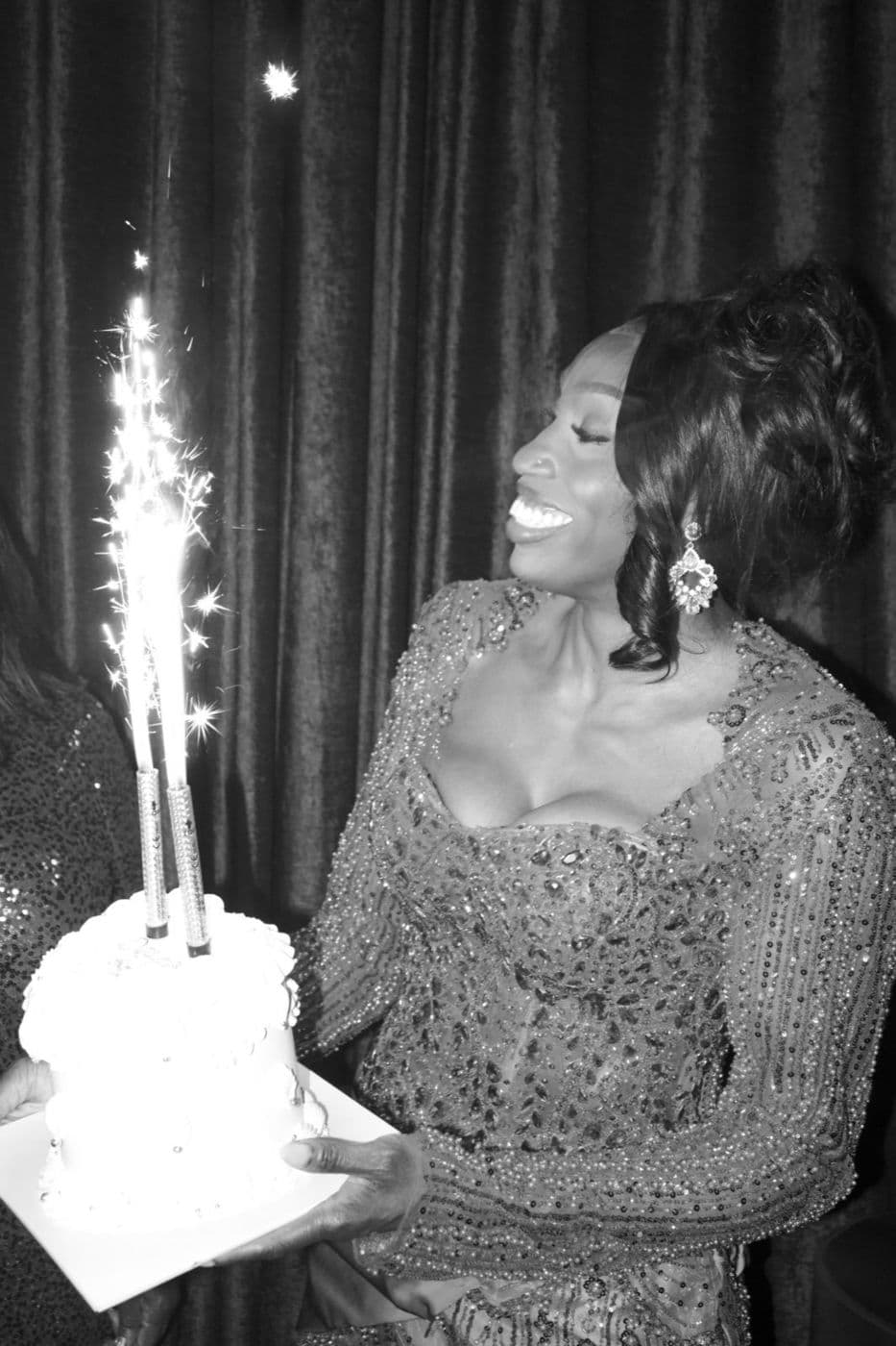 Black and white. A woman holding a cake lit by a sparkler.