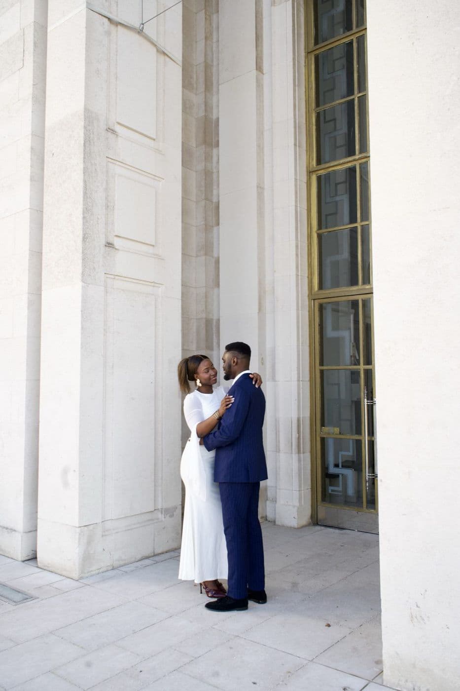 A couple at a distance between tall stone columns, one in white and one in navy.