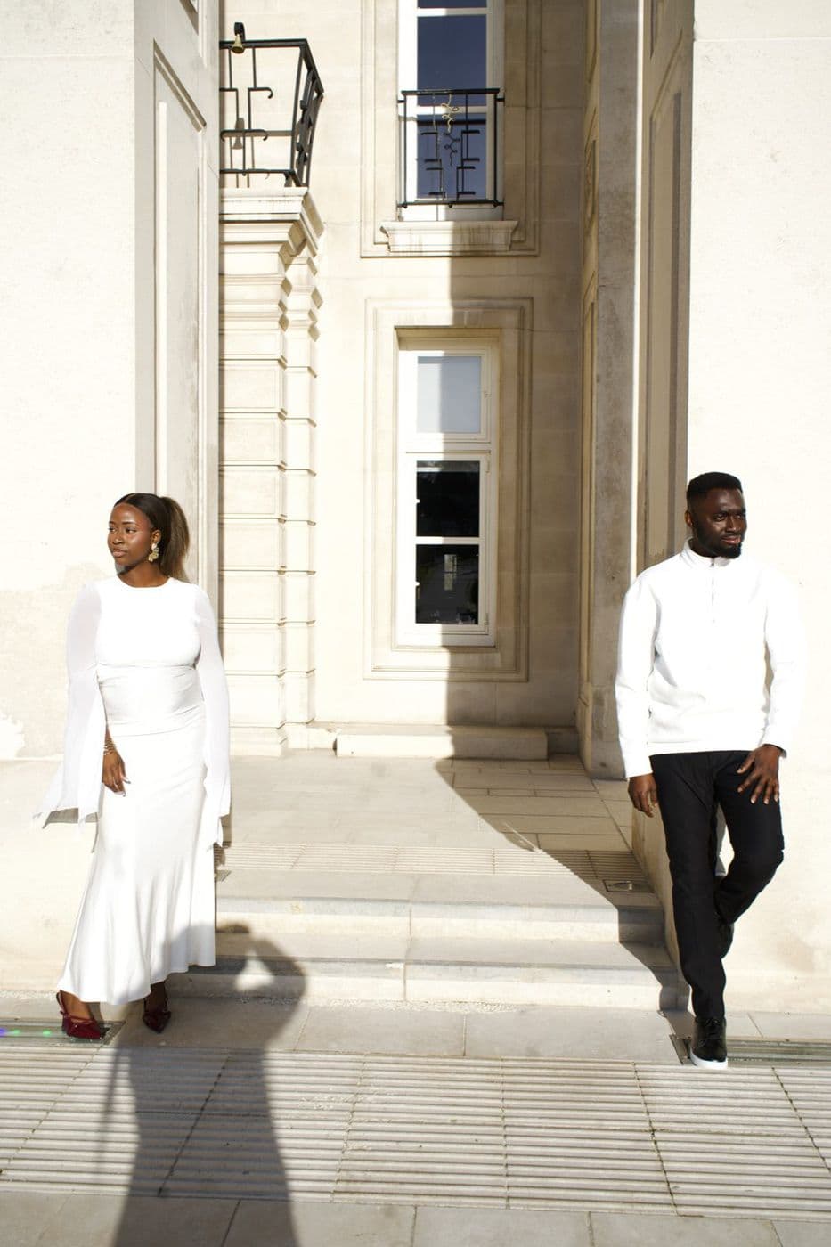 A couple walking apart down a stone colonnade in bright sunlight.