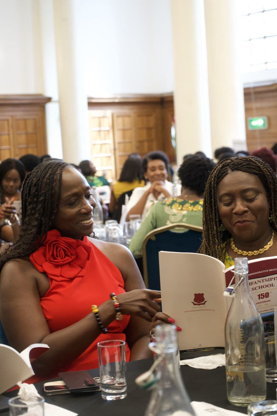 Two women seated at a long table, reading printed programmes.