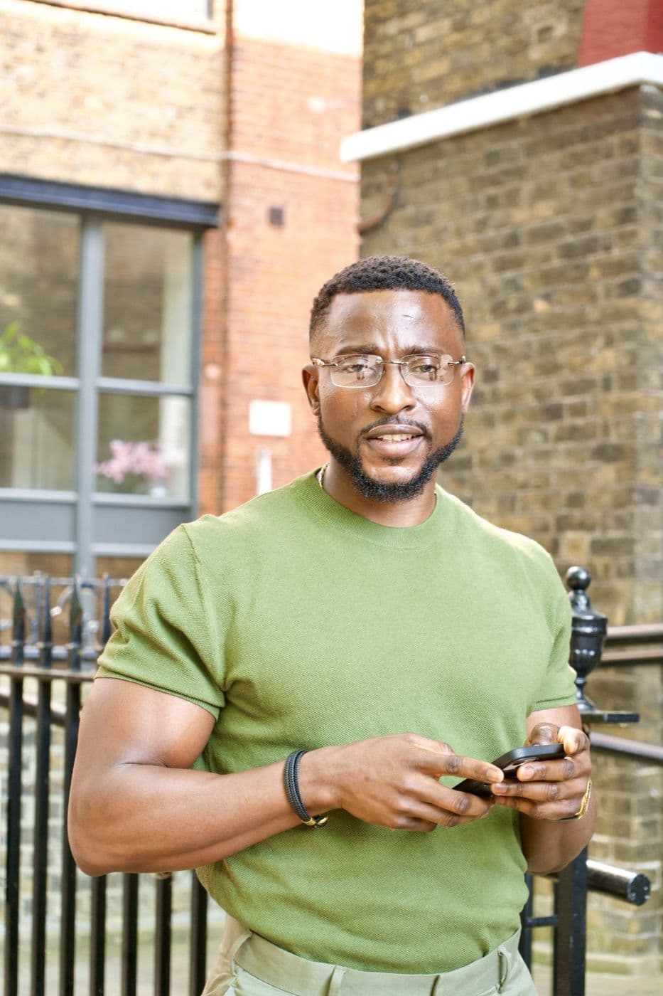 A man in a green shirt holding a phone, standing beside black railings.